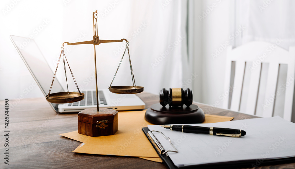 Justice and law concept.Male judge in a courtroom with the gavel, working with, computer and docking keyboard, eyeglasses, on table in morning light Justice and law concept.Male judge in a courtroom with the gavel, working with, computer and docking keyboard, eyeglasses, on table in morning light