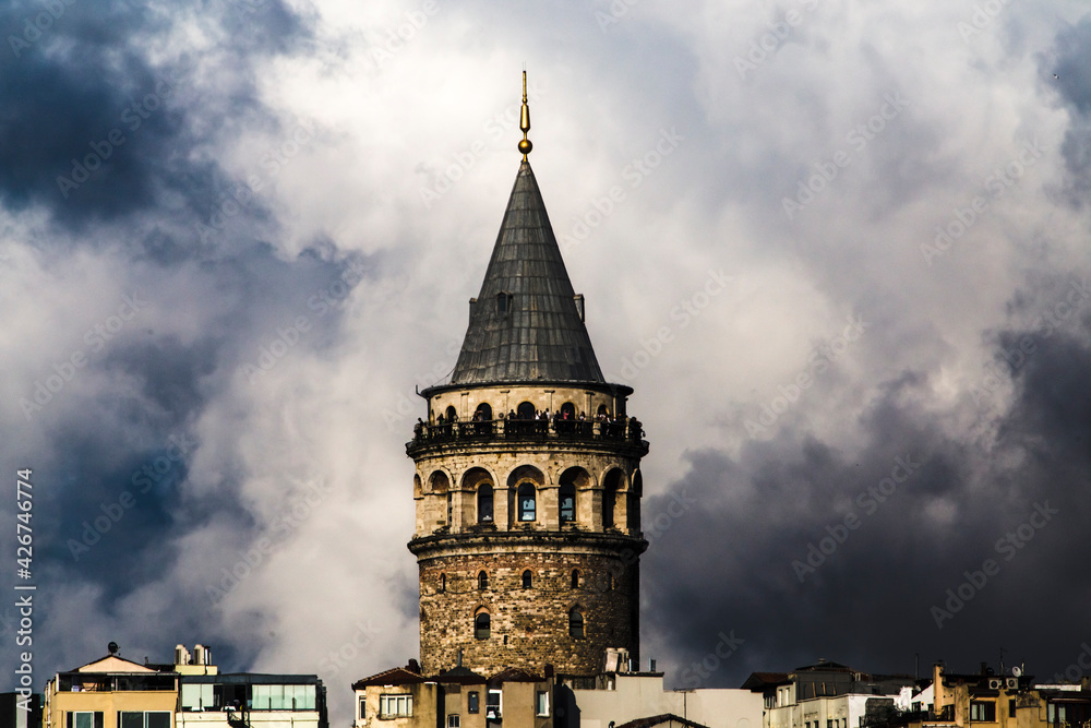 Fototapeta premium Close up of Galata Tower's observation terrace with tourists and dome, with large cloudy sky brewing a storm in the background with large copy space.