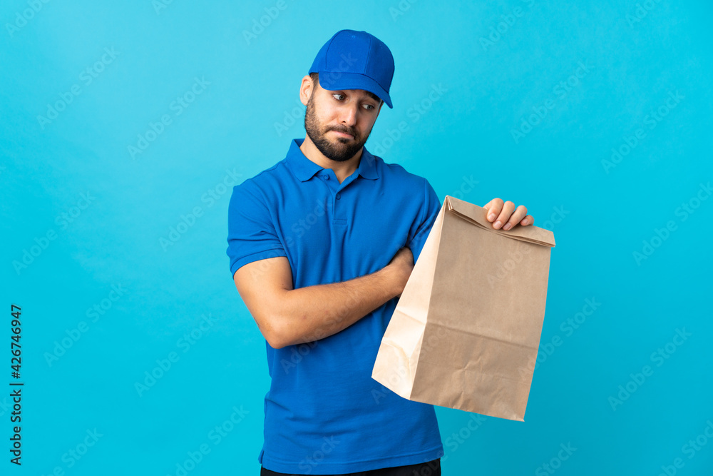 Delivery man with beard isolated on blue background with sad expression Delivery man with beard isolated on blue background with sad expression