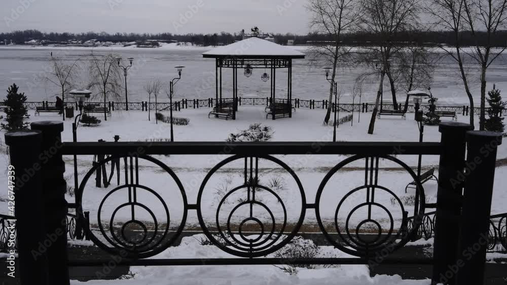 Park under snow against the background of the frozen river, lonely person walks slowly