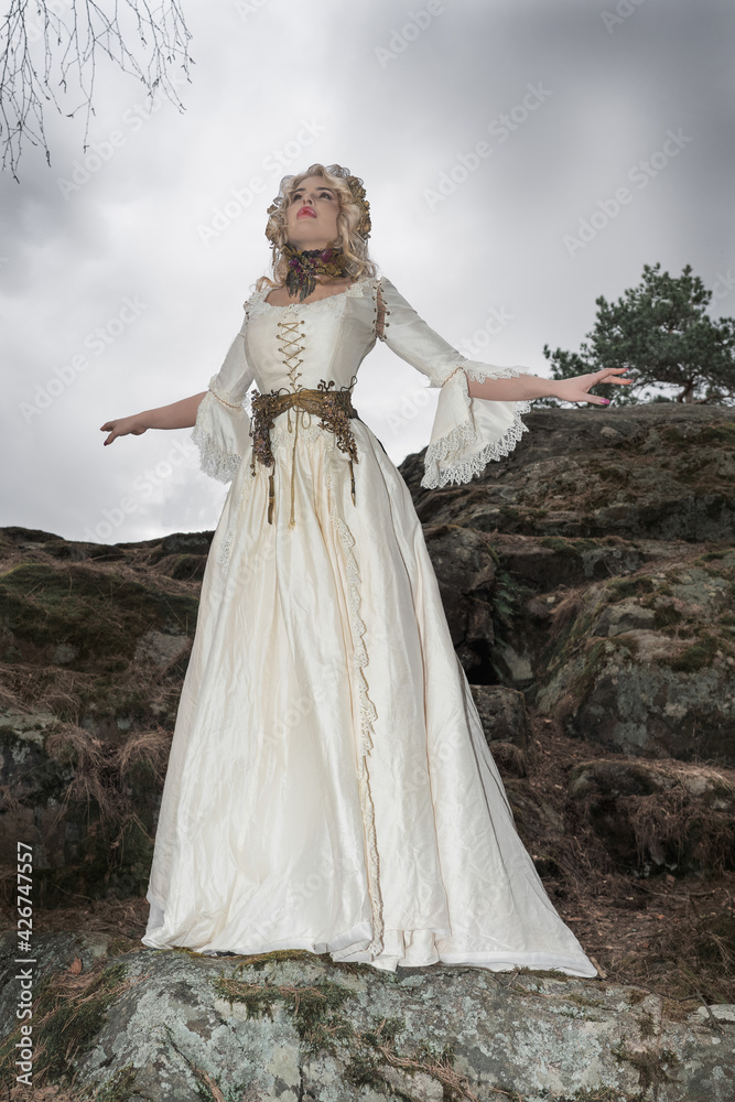 A gorgeous woman, a mythical creature, a queen, she is in a white dress, on large stones, in the autumn forest The concept of a fairy tale, legend, theater, cinema A gorgeous woman, a mythical creature, a queen, she is in a white dress, on large stones, in the autumn forest The concept of a fairy tale, legend, theater, cinema