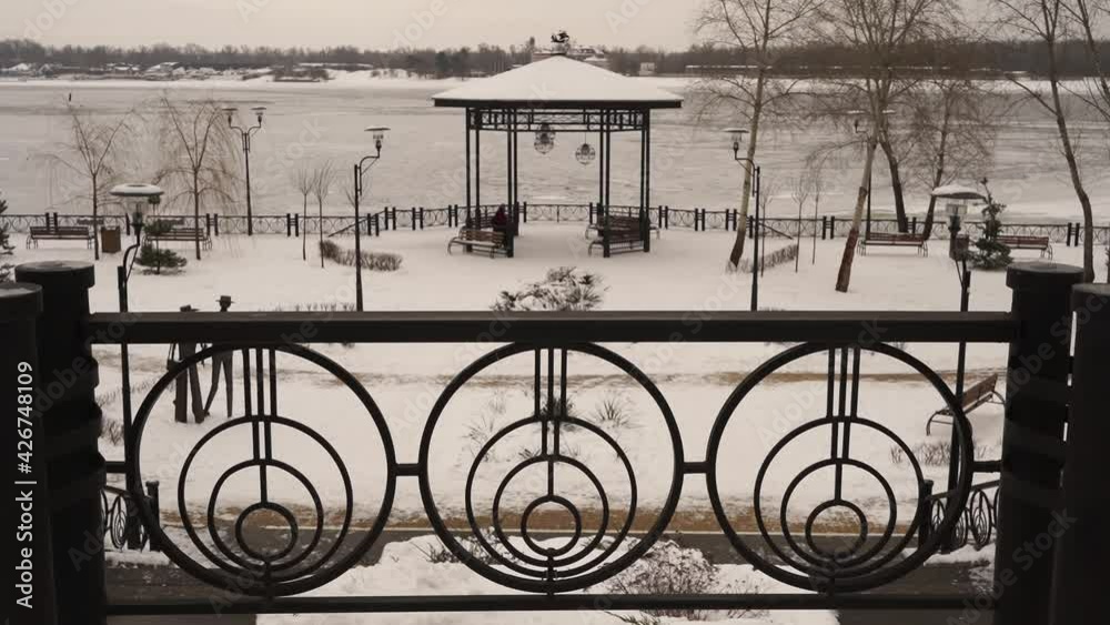 Park under snow against the background of the frozen river, lonely person walks slowly