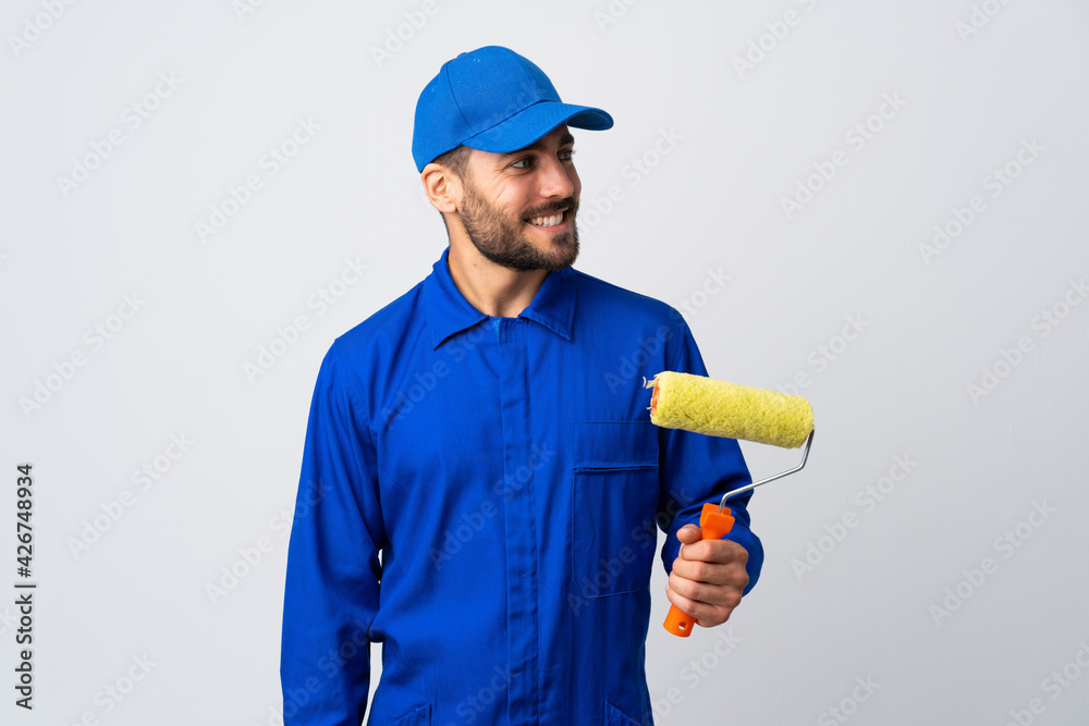 Painter man holding a paint roller isolated on white background looking to the side and smiling Painter man holding a paint roller isolated on white background looking to the side and smiling