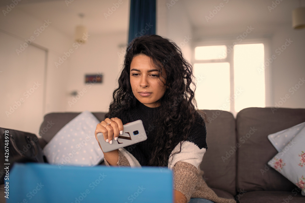 Woman working from home with smart phone and laptop on sofa Woman working from home with smart phone and laptop on sofa