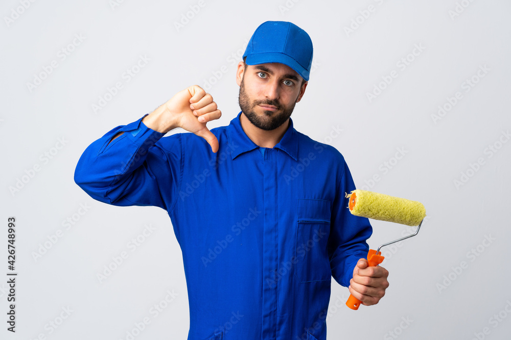 Painter man holding a paint roller isolated on white background showing thumb down with negative expression