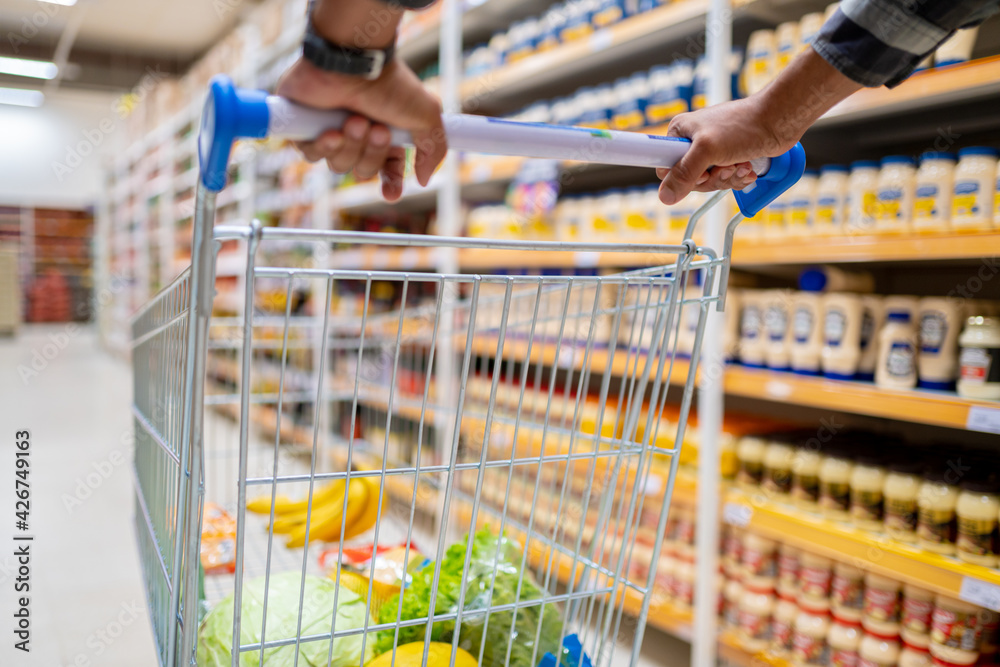 man's hand holds the shopping cart from the supermarket with blurred background