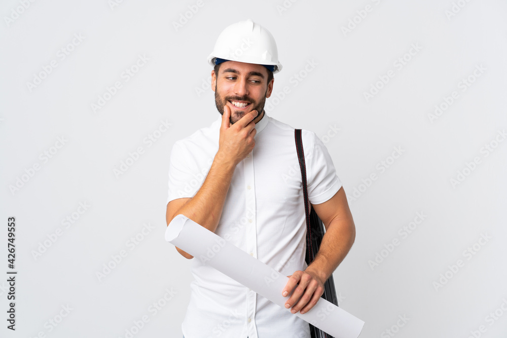 Young architect man with helmet and holding blueprints isolated on white background looking to the side and smiling Young architect man with helmet and holding blueprints isolated on white background looking to the side and smiling