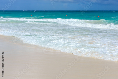 A foamy wave runs over the sandy beach. Seascape turquoise ocean and sandy coast against the blue sky. Rest by the sea. Exotic island.