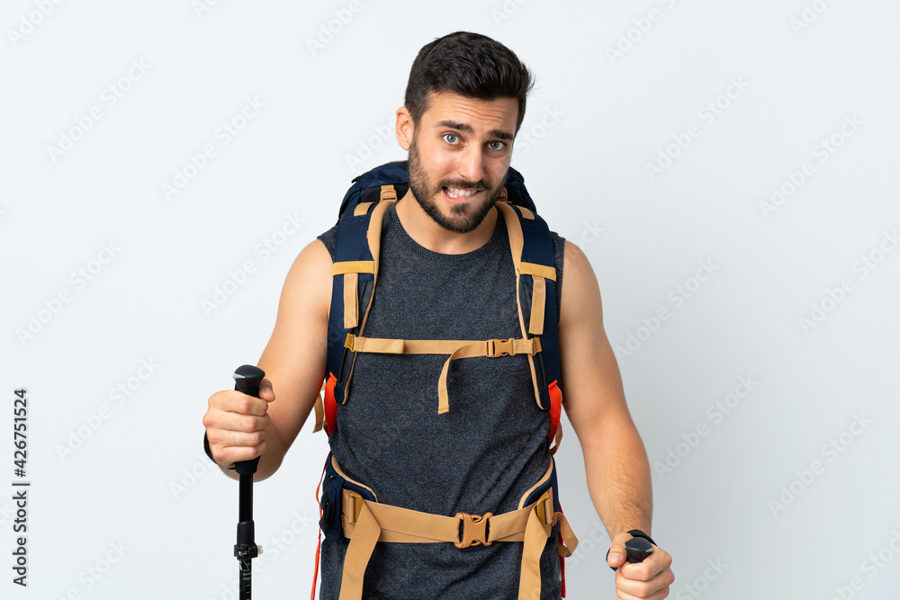 Young mountaineer man with a big backpack and trekking poles isolated on white background having doubts and with confuse face expression