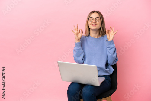 Young woman sitting on a chair with laptop over isolated pink background in zen pose © luismolinero