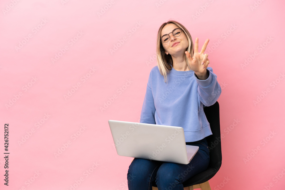 Young woman sitting on a chair with laptop over isolated pink background happy and counting three with fingers Young woman sitting on a chair with laptop over isolated pink background happy and counting three with fingers