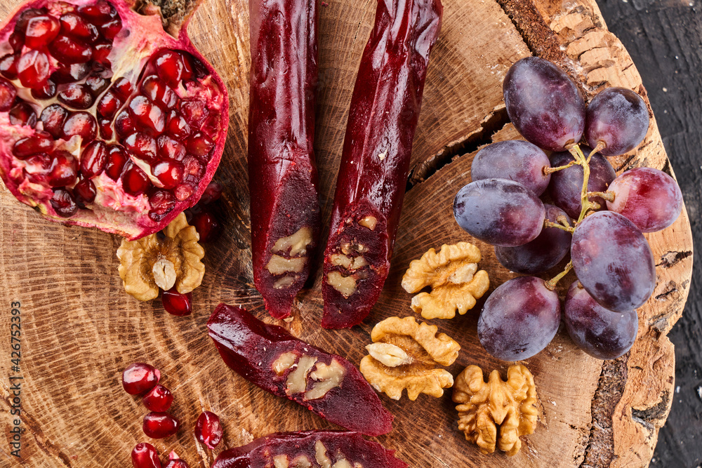 slicing Churchkhela, pomegranate, grapes and nuts on a wooden background, top view, serving slicing Churchkhela, pomegranate, grapes and nuts on a wooden background, top view, serving