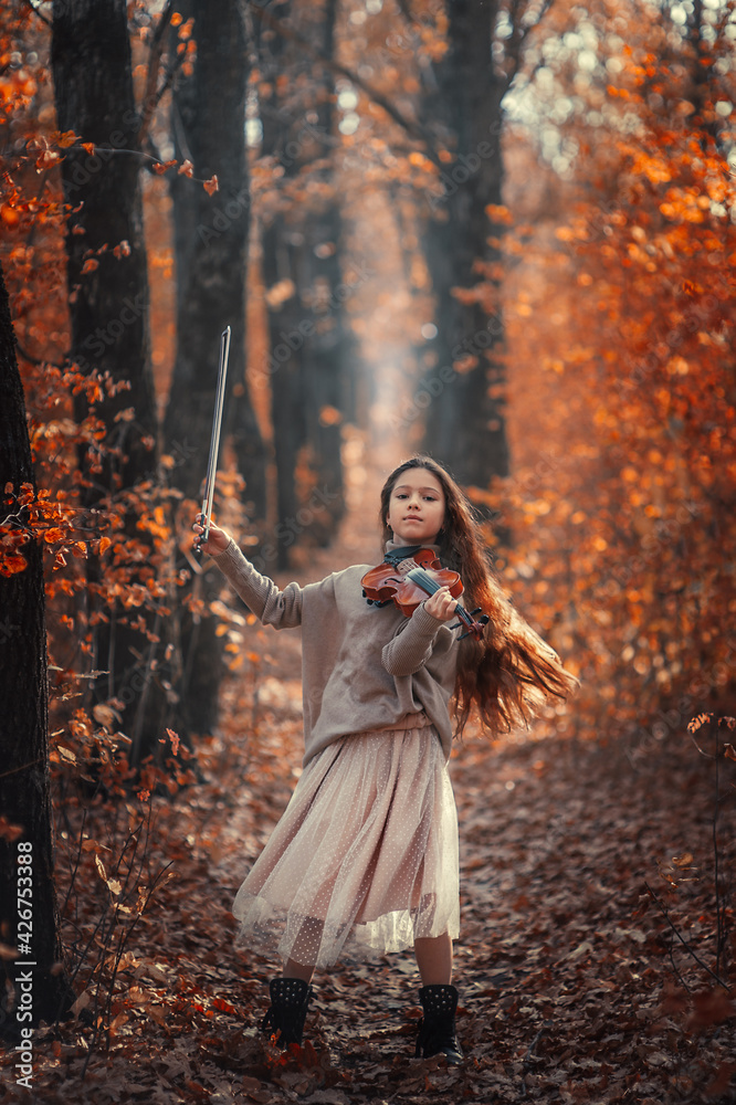 A beautiful girl with long hair plays the violin in the autumn forest.