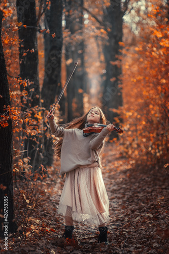 A beautiful girl with long hair plays the violin in the autumn forest.