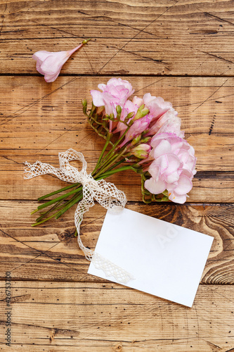 Blank card on a wooden table between pink flowers