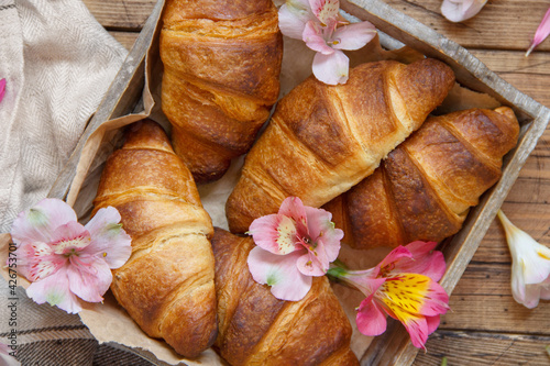 Fresh croissants and flowers in a tray on a wooden table