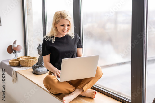 Remote work at home, freelance during covid-19 quarantine. Smiling lady sitting and working on laptop in cozy living room interior, free space