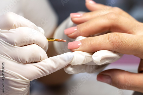 Manicure coating and strengthening of natural nails with artificial material gel in a beauty salon by a specialist. Close-up. Space for text
