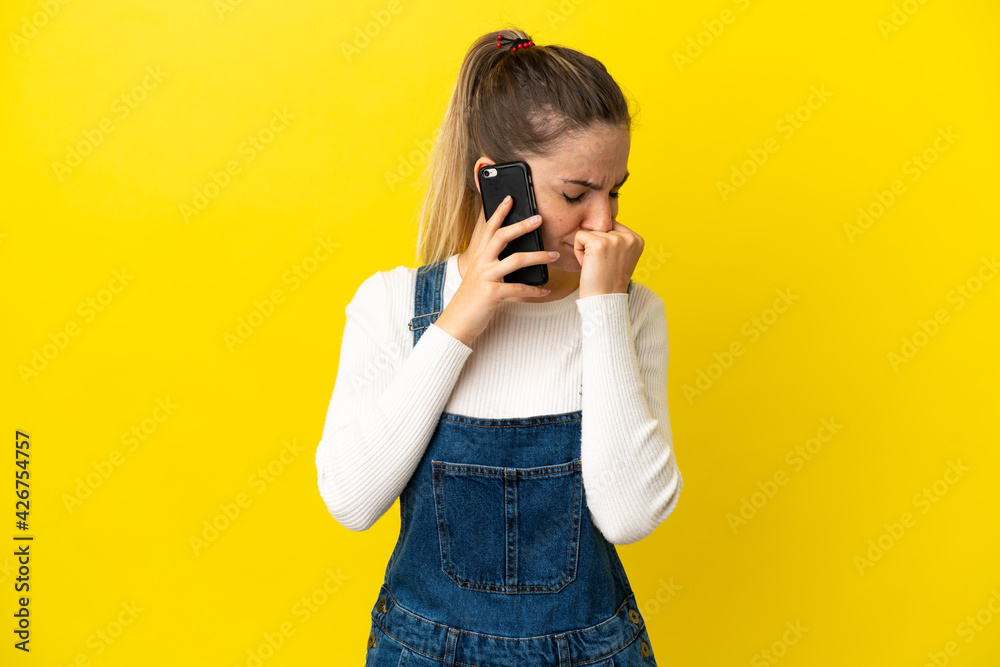 Young woman using mobile phone over isolated yellow background having doubts Young woman using mobile phone over isolated yellow background having doubts