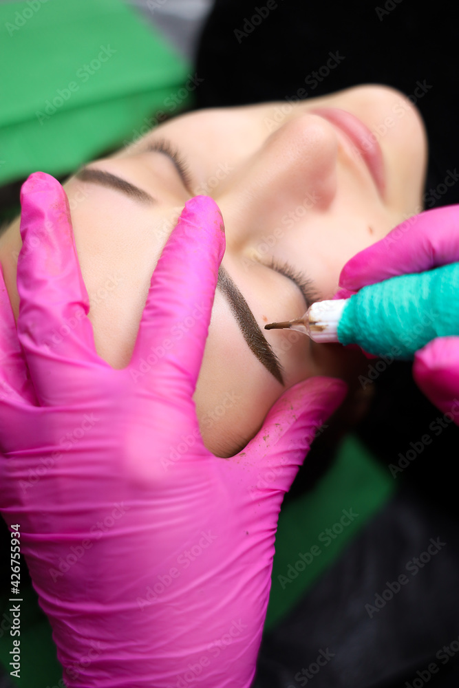 Powder coating of eyebrows in permanent makeup. The master performs eyebrow tattooing Powder coating of eyebrows in permanent makeup. The master performs eyebrow tattooing