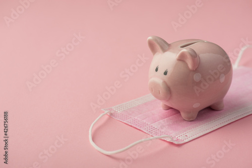 Closeup photo of piggy bank on medical mask isolated pink background with copyspace