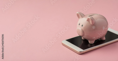 Closeup photo of piggy bank on smartphone isolated pink background with copyspace