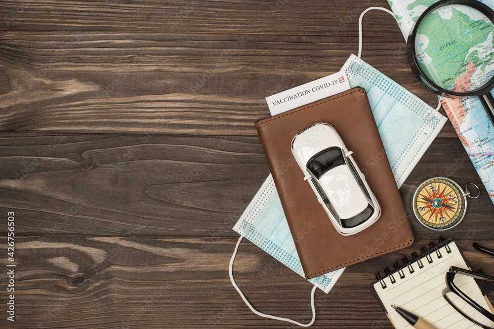 Overhead photo of brown passport with vaccination covid-19 test inside car mask map magnifier compass notepad pen and glasses isolated on the wooden backdrop with blank space