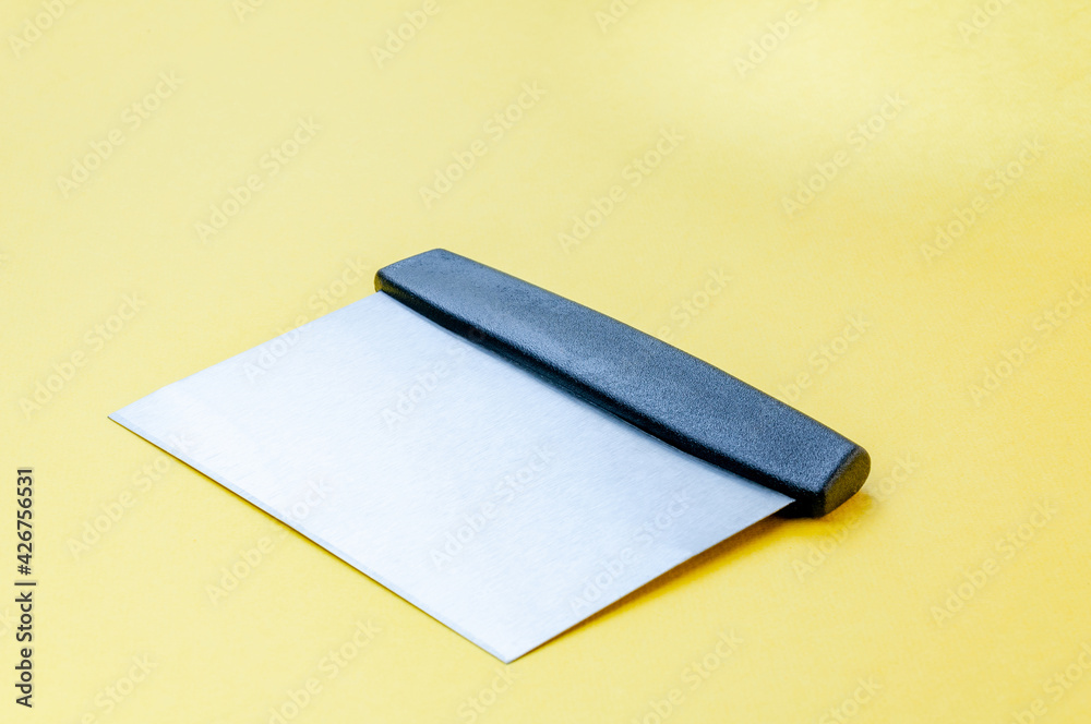 Metal dough scraper knife over bright yellow surface background. Stainless steel flat dough scraper with plastic handle - obrazy, fototapety, plakaty 