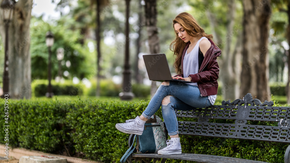 Young pretty woman works on laptop sitting on park bench near university close up Young pretty woman works on laptop sitting on park bench near university close up