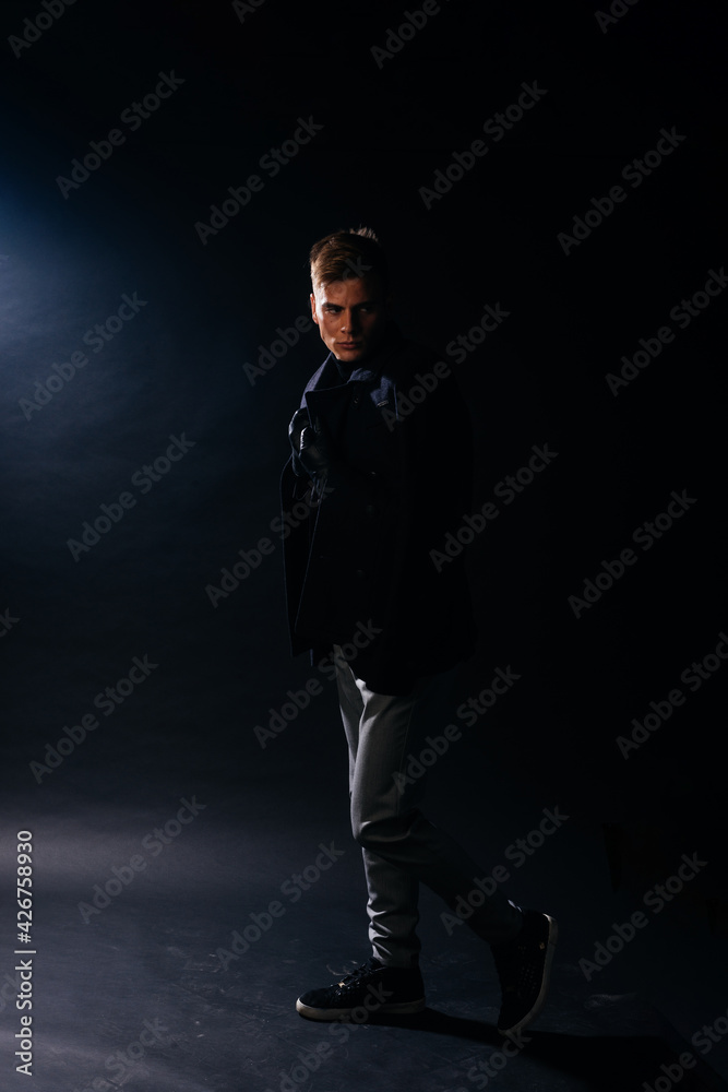 Portrait of a handsome with sharp jawline young man wearing a scarf while posing inside a studio on a black background.. Portrait of a handsome with sharp jawline young man wearing a scarf while posing inside a studio on a black background..