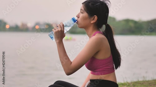 Young Asian woman drinking water after exercising at the park beside the river. Healthy lifestyle concept.