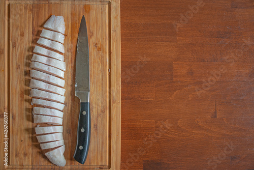 Half frozen fish at a wooden board cut on fine slices by a big knife, details, closeup, with copy space as a wooden table plate. Concept home cooking and healthy food.