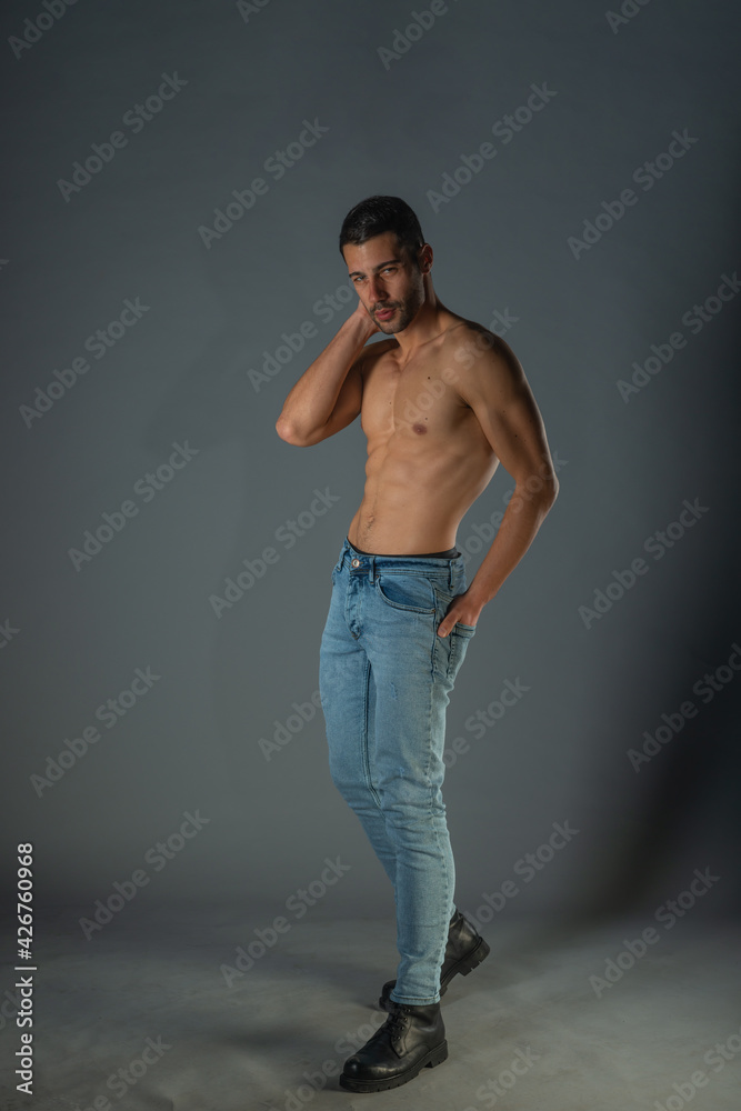 Full body portrait of sports man with denim jeans posing with bare torso in a dark studio Full body portrait of sports man with denim jeans posing with bare torso in a dark studio