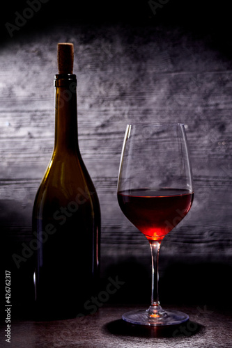 Glass with red wine and bottle on a dark background