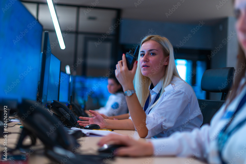 Happy security data center operator colleagues (coworkers) smiling and monitoring the CCTV footage while typing on a keyboard. Happy security data center operator colleagues (coworkers) smiling and monitoring the CCTV footage while typing on a keyboard.