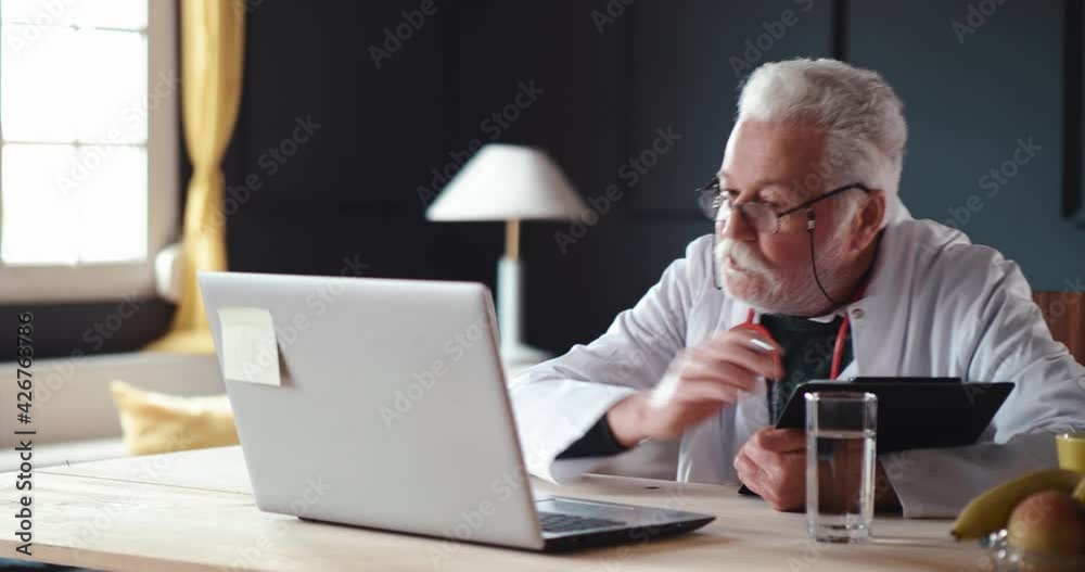Male old doctor writes the patient's therapy using a video call Male old doctor writes the patient's therapy using a video call