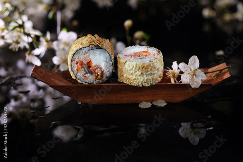Two rolls of tempura with rice, cheese and fish in a decorative, wooden boat on a black background. Japanese cuisine