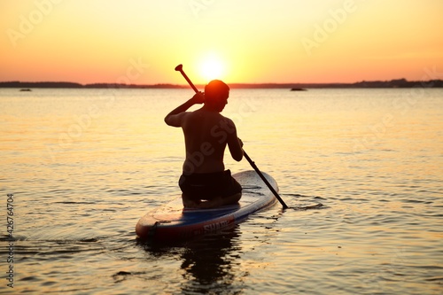 The man with a paddle stands on a sub board in the bay at sunset