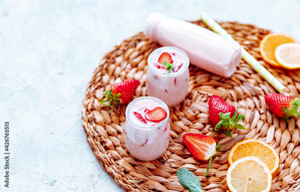 Milkshake with strawberries or drinking yogurt in a bottle with a beautiful straw with ripe strawberries and strawberry slices on a plain blue background. Milkshake with strawberries or drinking yogurt in a bottle with a beautiful straw with ripe strawberries and strawberry slices on a plain blue background.