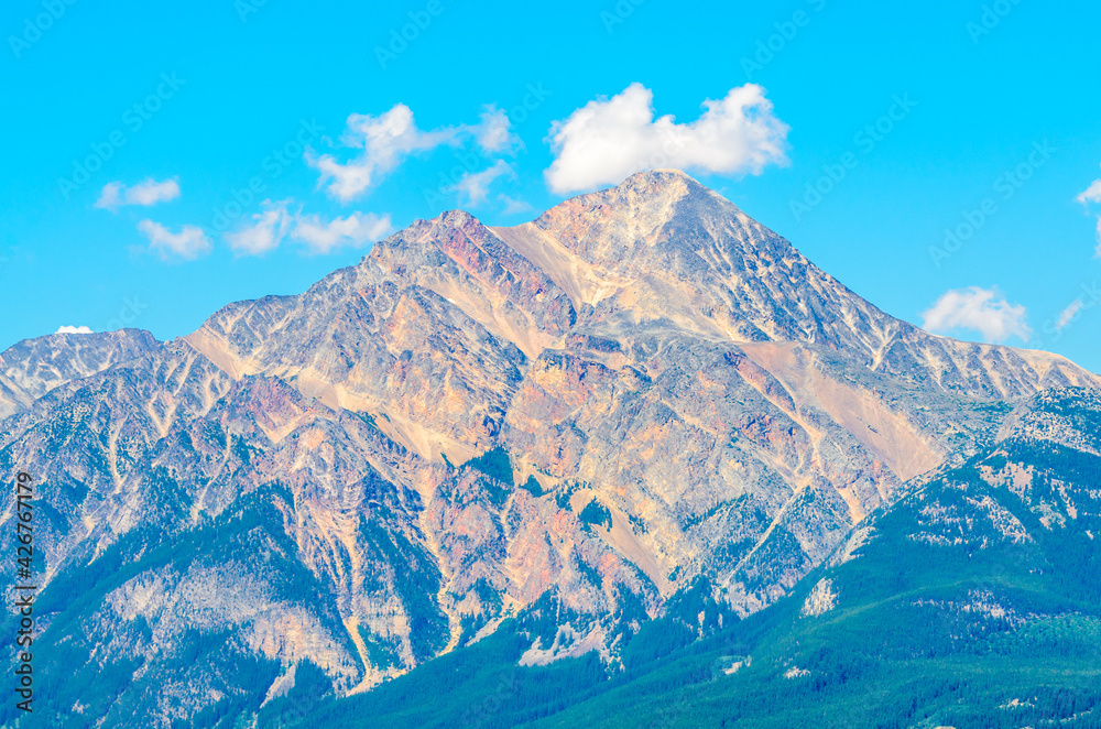 Scenery of high mountain peak over blue sky with white clouds.
