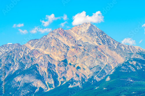 Scenery of high mountain peak over blue sky with white clouds.
