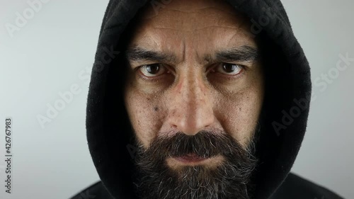 Attractive man with beard wearing black hoodie with seroius face looking at the camera. Close-up slow motion.