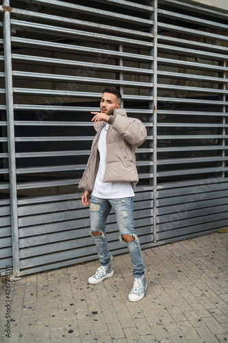 Chico joven guapo tatuado posando en la calle con conjutnos de moda