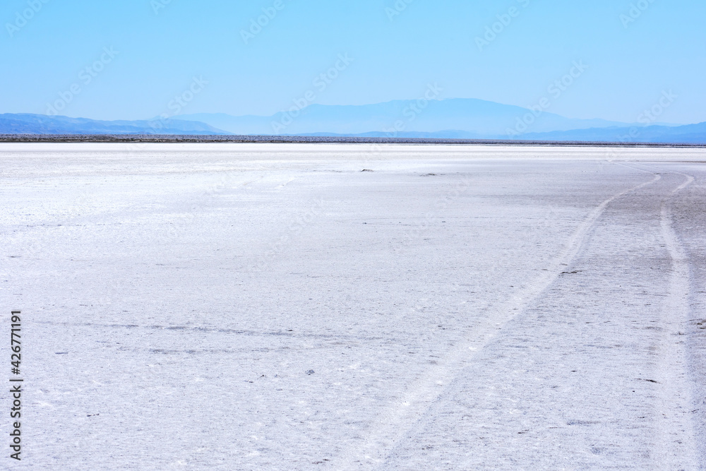 Obraz premium Car tire tracks lead into distant mountain ridge across dry lake bed of Soda Lake at Carrizo Plain National Monument, California.