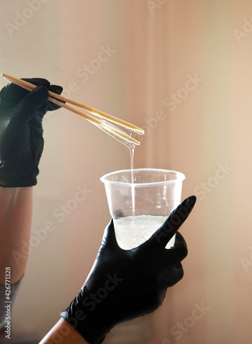 Epoxy resin, a girl in gloves painstakingly mixes the liquid in a plastic cup, against the window.