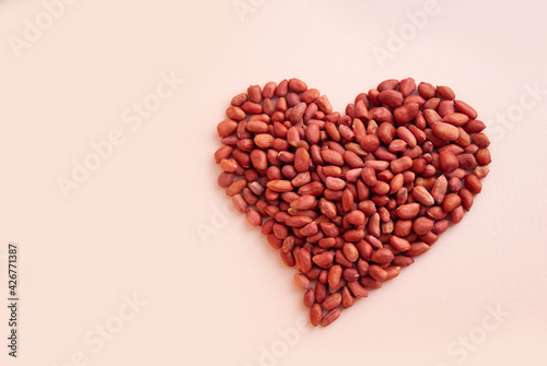 The peanuts are laid out in the shape of a heart. Raw groundnuts on a pastel background. Top view.