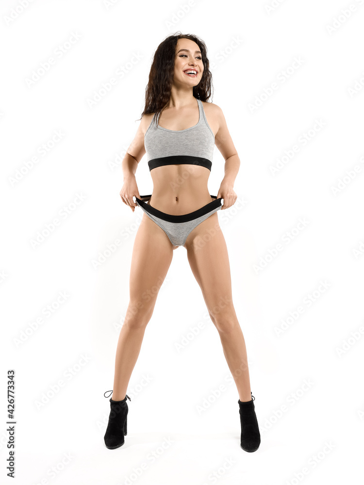 A young attractive, smiling, happy, flirtatious brunette in gray underwear with a toned athletic body is standing straight, pulls her panties. Isolated on white background A young attractive, smiling, happy, flirtatious brunette in gray underwear with a toned athletic body is standing straight, pulls her panties. Isolated on white background