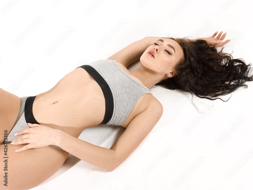 A young attractive brunette in gray underwear with a toned athletic body lies on her back in a relaxed position. Isolated on white background A young attractive brunette in gray underwear with a toned athletic body lies on her back in a relaxed position. Isolated on white background
