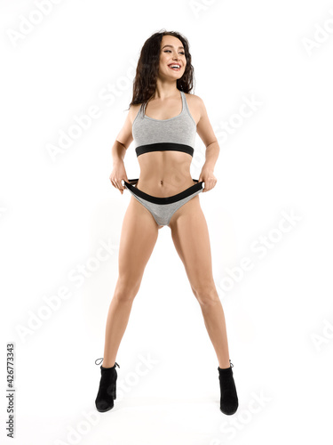 A young attractive, smiling, happy, flirtatious brunette in gray underwear with a toned athletic body is standing straight, pulls her panties. Isolated on white background