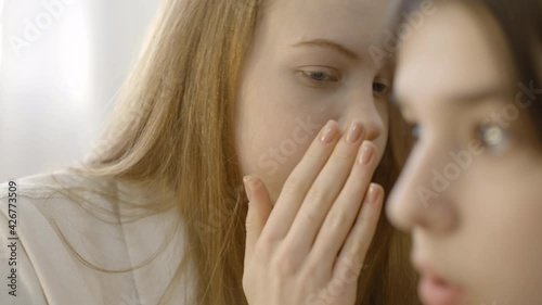 Teenage girl showing silence sign and telling secret to shocked female friend